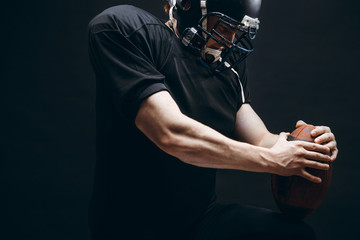 Fototapeta na wymiar American football player with black helmet and armour running in motion, holding ball, getting ready to score a goal, close up shot over dark background