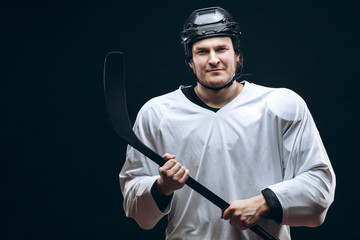 Hockey player wearing white protective gear and black helmet posing at camera with the hockey...