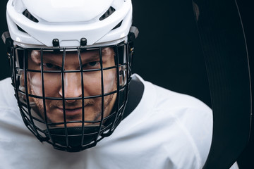 Face portrait of goalkeeper in hockey uniform and protective headgear over black background