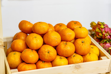 Tangerines with leaves and twigs are in a wooden box in the store on the shelf.