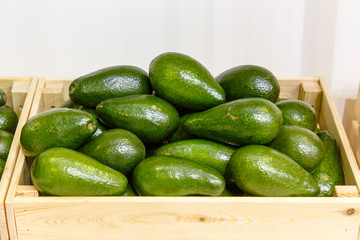 Fresh avocado are in a wooden box in the store on the shelf.