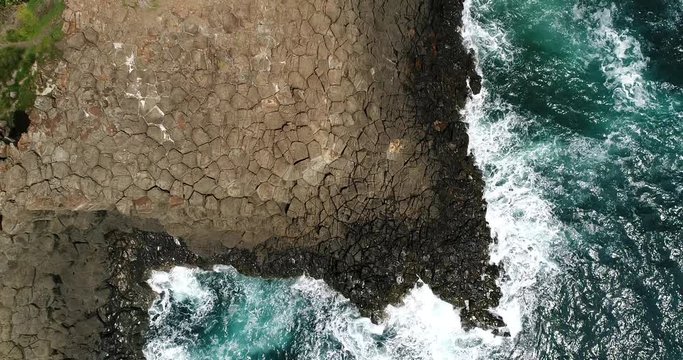 Edge of Pacific ocean sea bay at Bombo headland framed by hexagonal basalt pinnacle rocks in aerial top down view rising up from surface.
