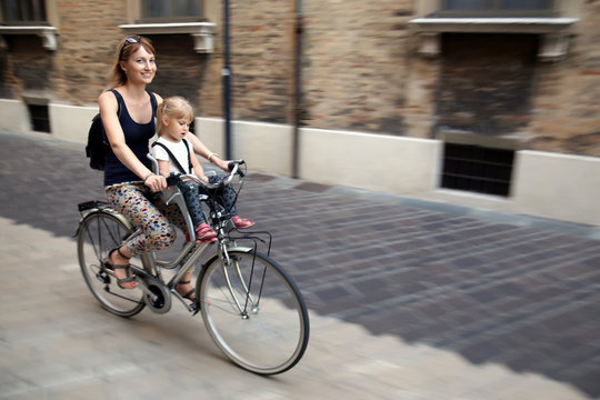 Mom with daughter riding bike in Italy. Child sitting in safety