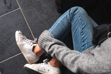 Top view image of a woman wearing jean and white sneakers touching her leg while sitting on the...