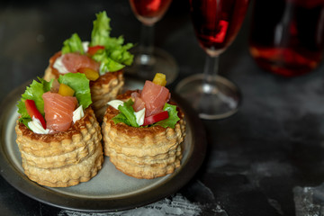 French cuisine, crunchy patties with lettuce and smoked salmon on a dark, rustic background, next to a glass of red wine