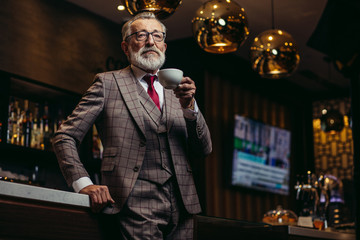 Portrait of wealthy prosperious senior businessman in drinking coffee near bar counter at elite...