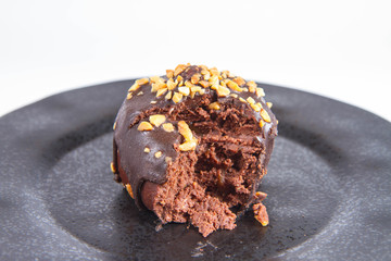 Rum ball decorated with chocolate and nuts on a black plate, partially eaten, on a white background