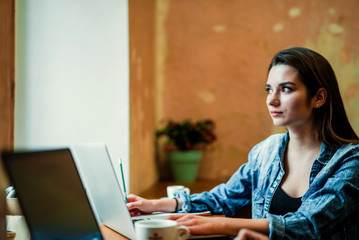 Young female student sits near the window with laptop and look through the window.