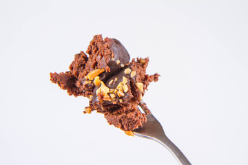 Rum ball decorated with chocolate and nuts on a fork on a white background
