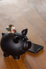 black piggy bank with several euros and a smartphone