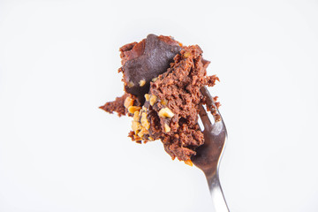 Rum ball decorated with chocolate and nuts on a fork on a white background