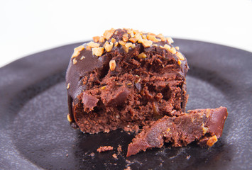 Rum ball decorated with chocolate and nuts on a black plate, partially eaten, on a white background