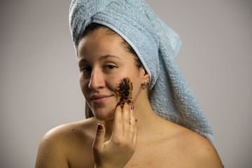 Young woman after shower with a towel and smiling, face with homemade coffee cream