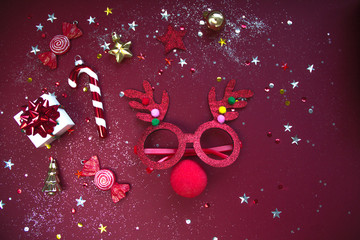 Reindeer face made of Christmas decoration on red background. Flat lay style. Festive concept.