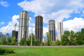 Obraz premium View through the green grass and the road to four multi-storey houses.