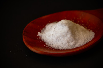 Salt on the wooden spoon with the dark background. Salt or Sodium chloride is a compound. It is frequently used for cooking.