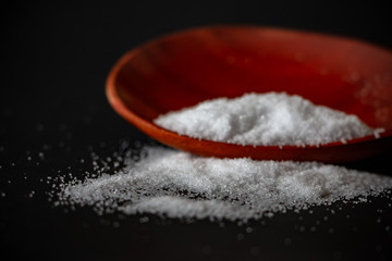 Salt on the wooden spoon with the dark background. Salt or Sodium chloride is a compound. It is frequently used for cooking.