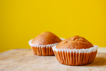 Closeup photo of the banana bread muffin in white paper cup on wooden table with yellow background. The homemade easy bake oven cake.