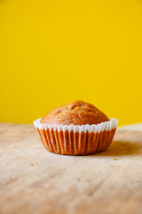 Closeup photo of the banana bread muffin in white paper cup on wooden table with yellow background. The homemade easy bake oven cake.
