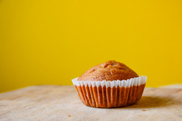 Closeup photo of the banana bread muffin in white paper cup on wooden table with yellow background. The homemade easy bake oven cake.