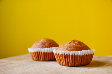 Closeup photo of the banana bread muffin in white paper cup on wooden table with yellow background. The homemade easy bake oven cake.