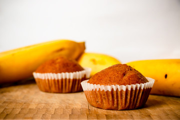 Closeup photo of the banana bread muffin in white paper cup and the bananas on wooden background. The homemade easy bake oven cake.