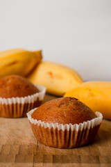 Closeup photo of the banana bread muffin in white paper cup and the bananas on wooden background. The homemade easy bake oven cake.