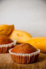 Closeup photo of the banana bread muffin in white paper cup and the bananas on wooden background. The homemade easy bake oven cake.