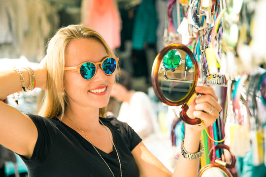 joung beautiful blond woman on the market are looking for some gifs, sunglasses and bags. she is shopping on a sunny day in italy on her travel