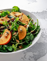 Persimmon and pea shoot salad with walnuts, pomegranate and pumpkin seed in a white table