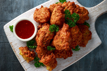 Crispy onion bhajis with sweet chilli sauce on white wooden board