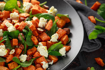 Healthy roasted sweet potato salad with spinach, feta cheese, hazelnut nuts in black plate, rustic background