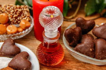 Bottle of perfume and various of cookies on wooden table with red candle. Home liana in the background. Close up.