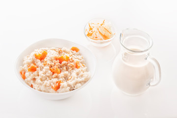Fototapeta na wymiar Oatmeal with pumpkin and nuts in a plate, vegetable salad and a glass jug with milk on a white background. Close-up. Copy space