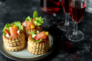 French cuisine, crunchy patties with lettuce and smoked salmon on a dark, rustic background, next to a glass of red wine