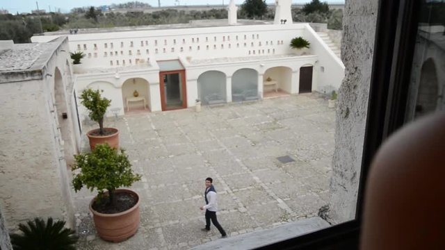 giovane donna osserva dalla finestre il suo uomo che esce dal cortile di casa 