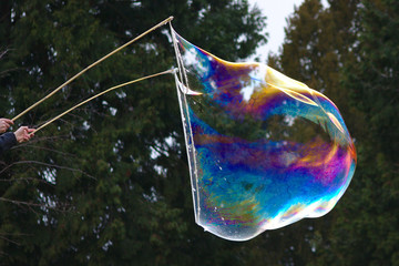 Gigantische Seifenblase schillert wie ein Regenbogen in prächtigen Farben im Sonnenschein