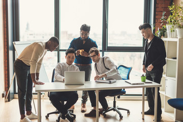 Multiracial male staff of architectural and design bureau communicating in modern loft office with...