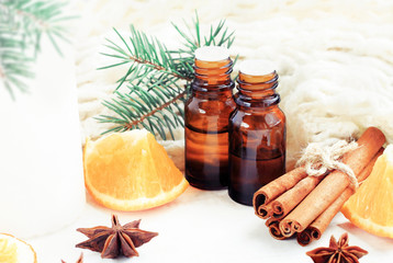 Relaxing winter season Essential oils blend. Dark glass bottles, cinnamon, orange, pine twigs, anise, woolen cloth. Natural home deodorants. White soft background.