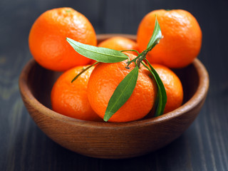 Tangerines with leaves in a wooden plate on a dark wooden table