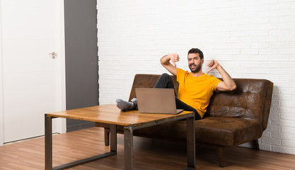 Man with his laptop in a room showing thumb down with both hands