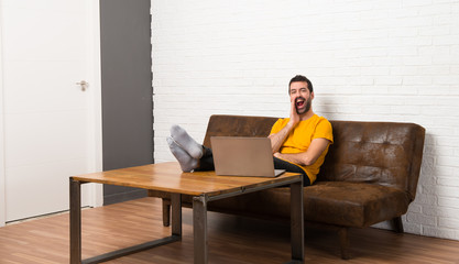 Man with his laptop in a room shouting with mouth wide open to the lateral