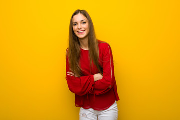 Young girl with red dress over yellow wall keeping the arms crossed while smiling