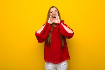 Young girl with red dress over yellow wall shouting and announcing something