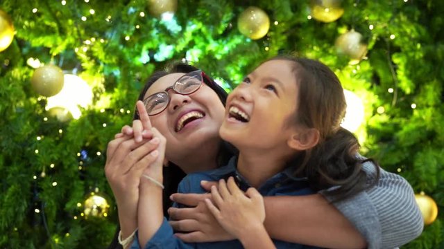 Little asian girl and mom looking Christmas tree with decoration lighting. Slow motion
