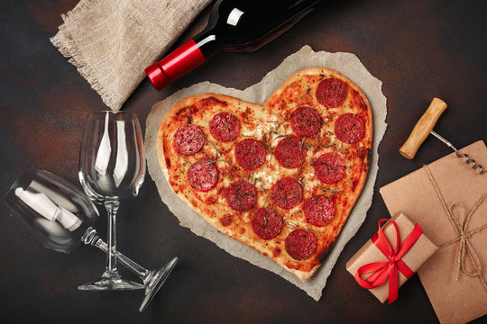 Heart shaped pizza with mozzarella, sausagered, wine bottle, two wineglass, gift box on rusty background