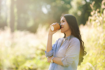 Young woman with cup of coffee on hand in the meadow at the morning time.