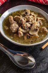 Soup with pieces of pork and mushrooms in bowl.