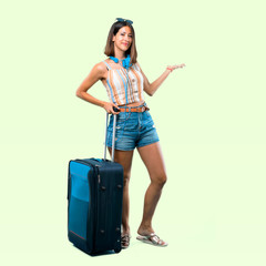 Full body of Girl traveling with her suitcase pointing back with the index finger presenting a product on isolated green background