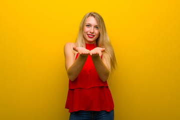Young girl with red dress over yellow wall holding copyspace imaginary on the palm to insert an ad